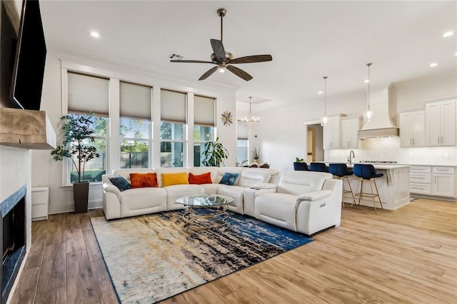 living room featuring ceiling fan with notable chandelier, recessed lighting, a fireplace, and light wood-style floors