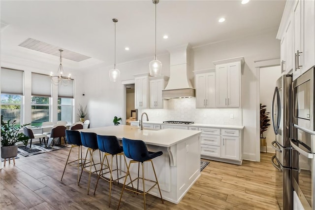 kitchen featuring a raised ceiling, decorative backsplash, light wood-style flooring, a kitchen breakfast bar, and premium range hood