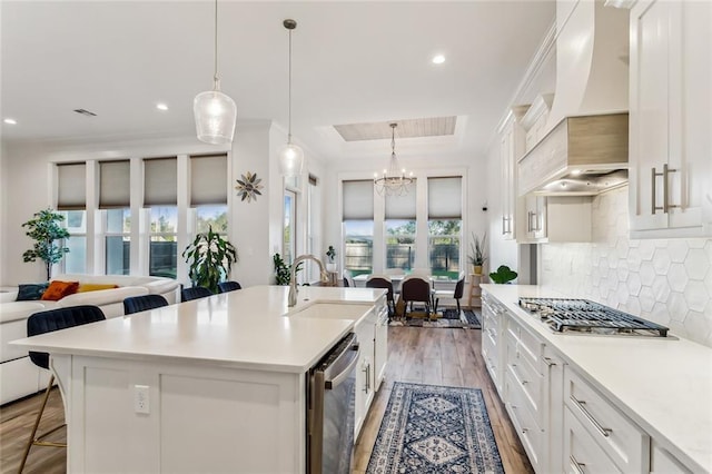 kitchen featuring a raised ceiling, light wood-style flooring, appliances with stainless steel finishes, premium range hood, and a kitchen breakfast bar