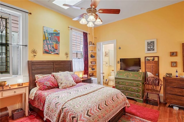 bedroom featuring hardwood / wood-style floors, ceiling fan, ensuite bathroom, and a skylight