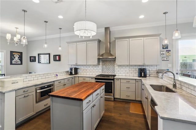 kitchen featuring kitchen peninsula, appliances with stainless steel finishes, pendant lighting, and wall chimney range hood