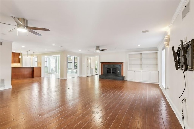 unfurnished living room featuring hardwood / wood-style flooring, built in shelves, ceiling fan, and ornamental molding