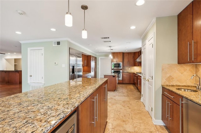 kitchen with light stone countertops, pendant lighting, built in appliances, and sink