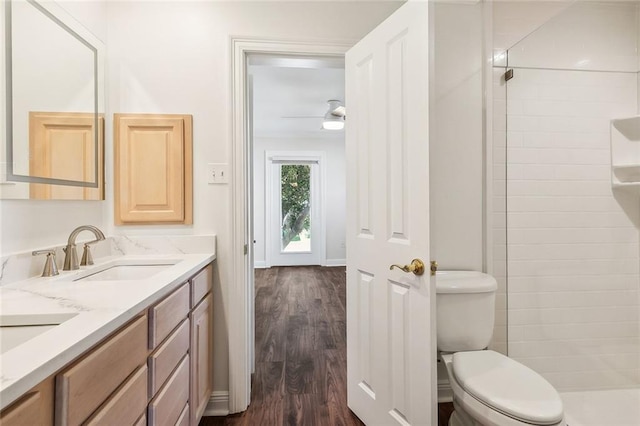 bathroom with hardwood / wood-style floors, vanity, ceiling fan, toilet, and tiled shower