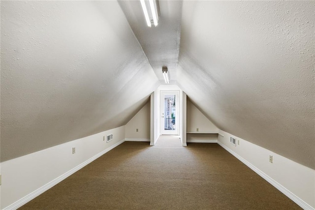 bonus room with a textured ceiling, vaulted ceiling, and dark colored carpet