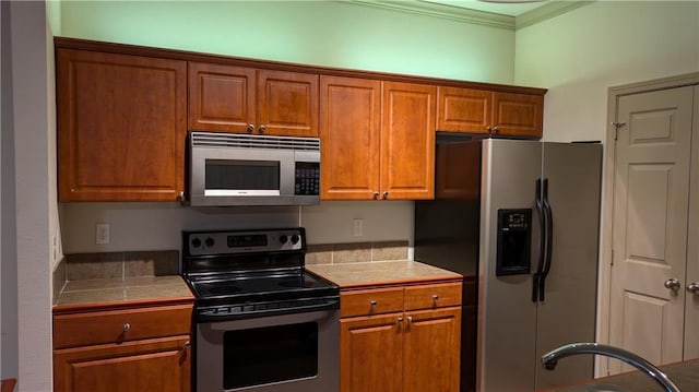 kitchen featuring crown molding, tile counters, and appliances with stainless steel finishes