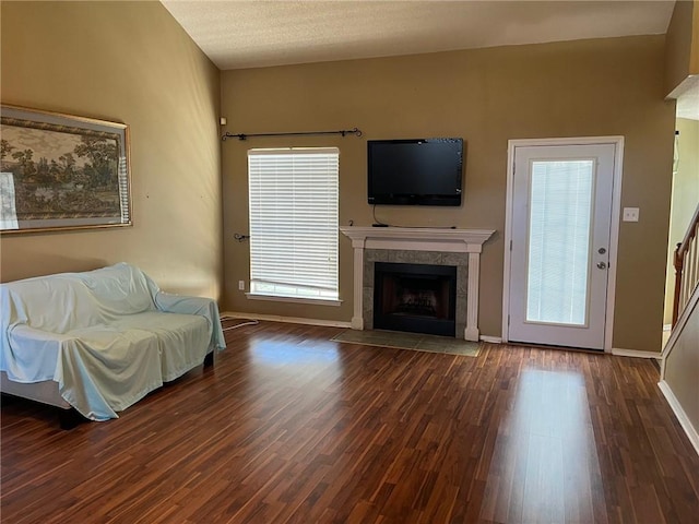 unfurnished living room with a textured ceiling, plenty of natural light, dark wood-type flooring, and a tiled fireplace