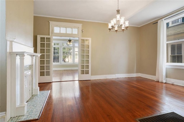 unfurnished dining area with french doors, ceiling fan with notable chandelier, dark hardwood / wood-style floors, and crown molding