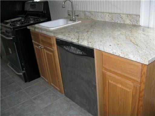 kitchen featuring light tile patterned flooring, sink, light stone counters, and black appliances