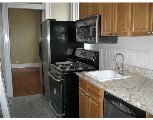 1127 Fern St, New Orleans, LA 70118 - kitchen featuring black appliances, a sink, brown cabinets, a wainscoted wall, and light stone countertops