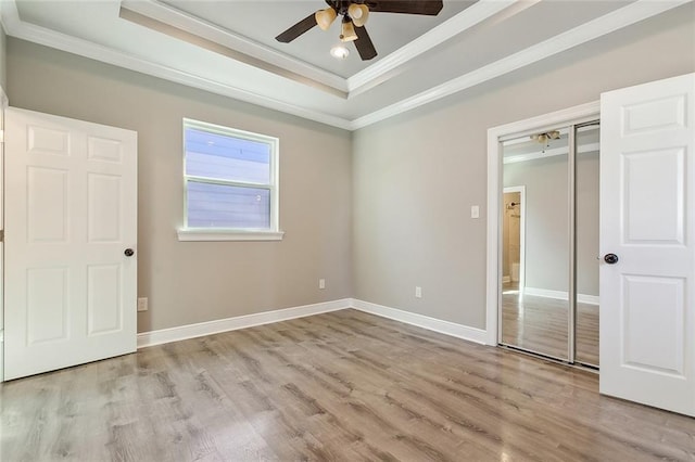 unfurnished bedroom with a tray ceiling, light wood-type flooring, and crown molding