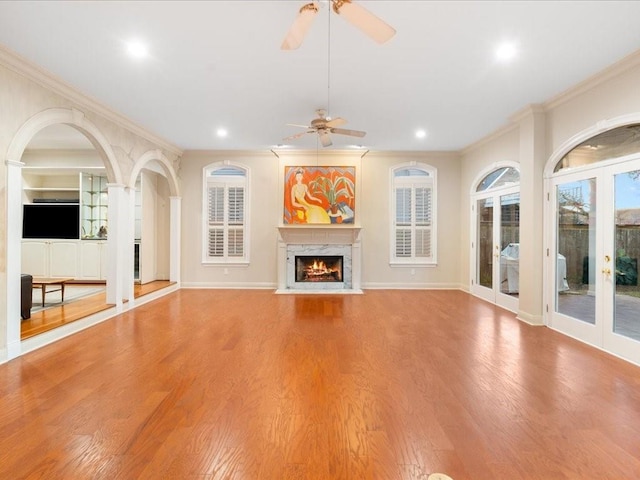 unfurnished living room featuring french doors, a high end fireplace, ornamental molding, and light hardwood / wood-style flooring