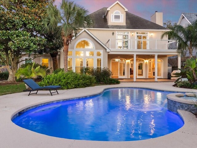 back house at dusk with a patio area, a swimming pool with hot tub, and a balcony