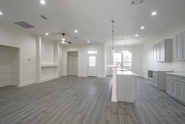 kitchen with gray cabinetry, ceiling fan with notable chandelier, dark hardwood / wood-style floors, and a kitchen island with sink