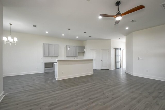 unfurnished living room with a barn door, ceiling fan with notable chandelier, and dark hardwood / wood-style floors