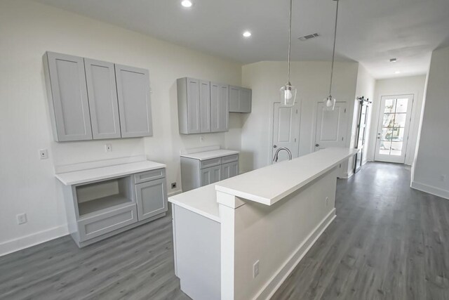 kitchen with gray cabinetry, decorative light fixtures, an island with sink, and dark wood-type flooring