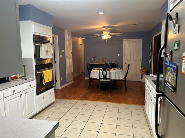 kitchen featuring ceiling fan, double oven, freestanding refrigerator, light tile patterned flooring, and white cabinetry