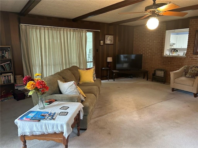 living area with beam ceiling, carpet floors, wooden walls, brick wall, and ceiling fan