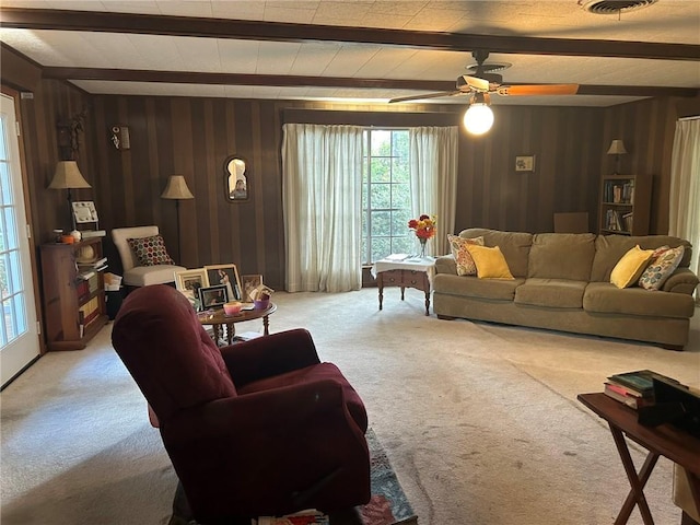 carpeted living area featuring beam ceiling, visible vents, wood walls, and ceiling fan