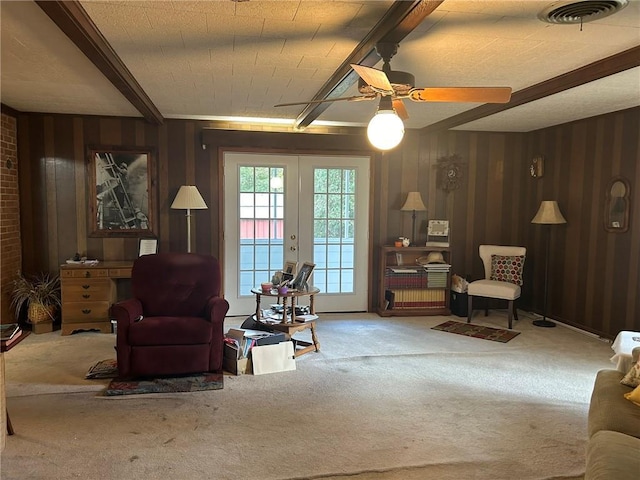 living area with visible vents, wooden walls, beamed ceiling, carpet floors, and a ceiling fan