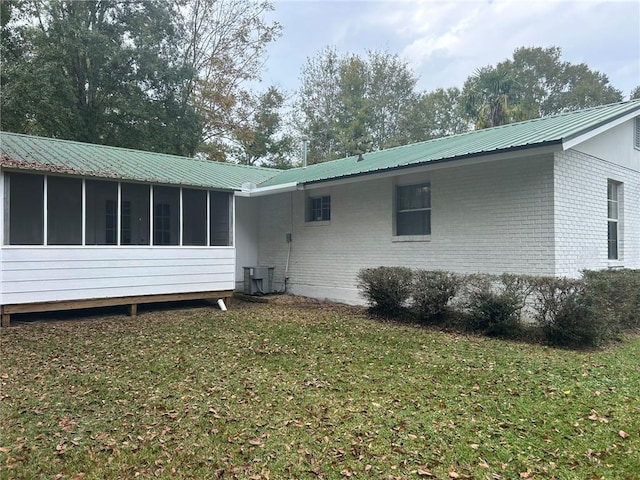 rear view of house with central AC, a sunroom, a lawn, brick siding, and metal roof