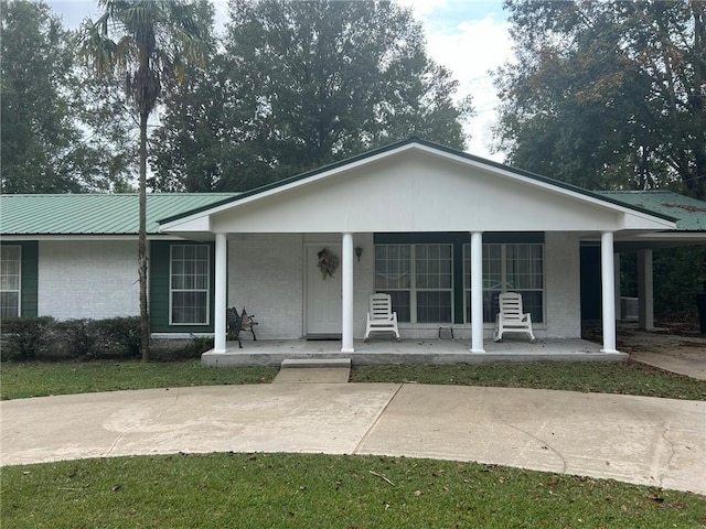 view of front of home featuring metal roof, brick siding, and covered porch