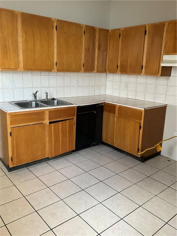 9009 Belfast St, New Orleans, LA 70118 - kitchen with tasteful backsplash, light countertops, a sink, under cabinet range hood, and brown cabinets