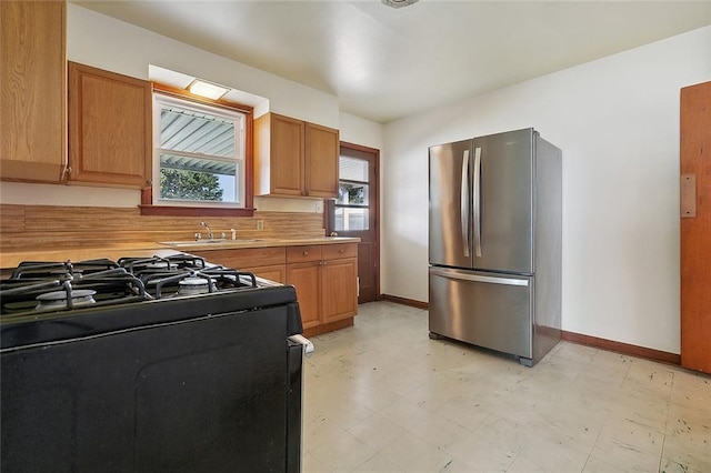 kitchen featuring stainless steel refrigerator, black gas stove, and sink