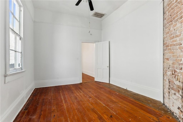 spare room featuring hardwood / wood-style flooring, ceiling fan, and brick wall