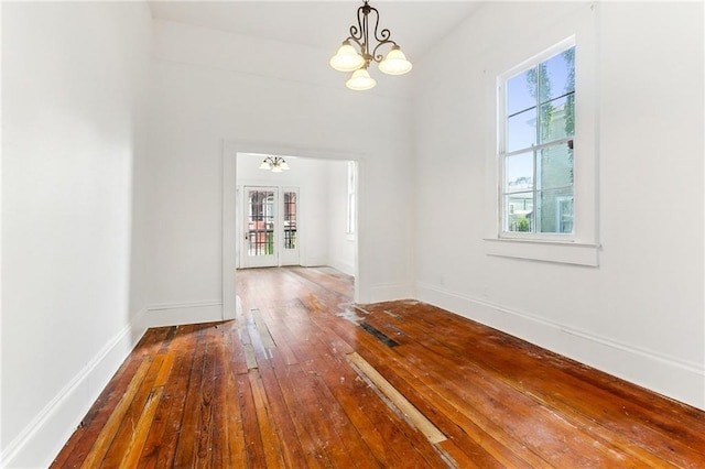 unfurnished dining area with hardwood / wood-style flooring, french doors, a wealth of natural light, and an inviting chandelier