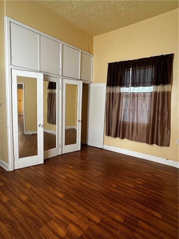 unfurnished bedroom featuring french doors, dark wood-type flooring, and a textured ceiling