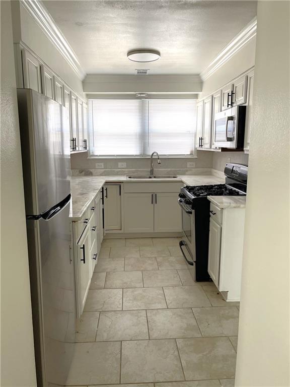 kitchen with crown molding, sink, light stone countertops, appliances with stainless steel finishes, and white cabinetry