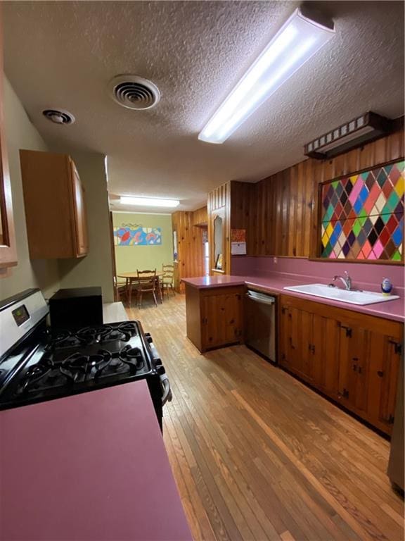 kitchen with stainless steel dishwasher, kitchen peninsula, black gas stove, light hardwood / wood-style floors, and a textured ceiling