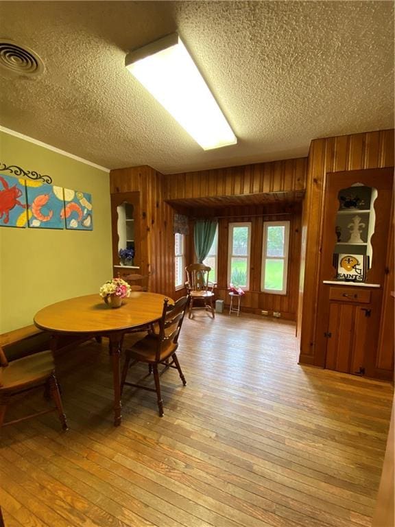 dining area featuring a textured ceiling, light hardwood / wood-style flooring, and wood walls