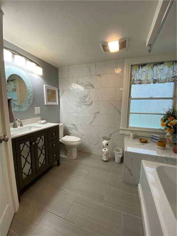 bathroom with tile patterned flooring, a bath, toilet, vanity, and tile walls