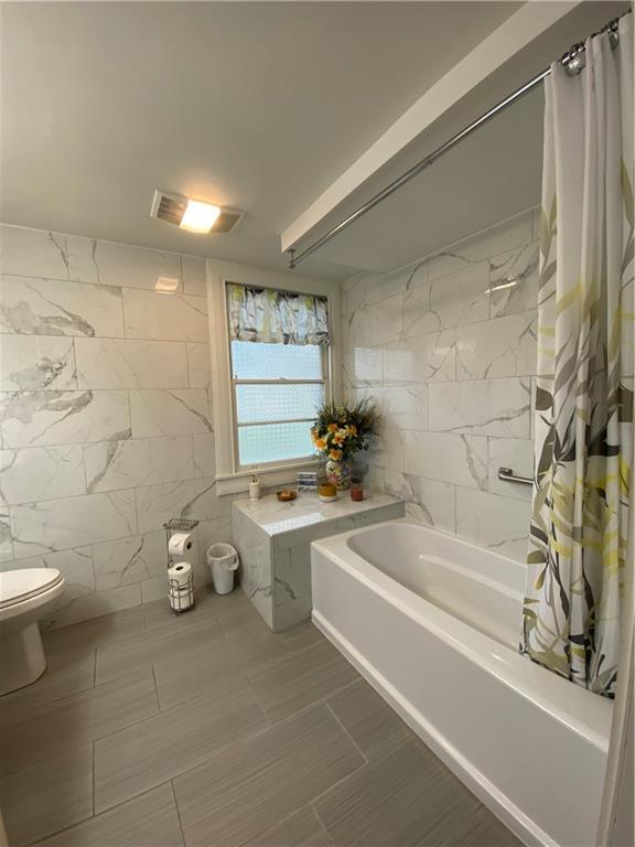 bathroom with shower / tub combo with curtain, tile walls, and toilet