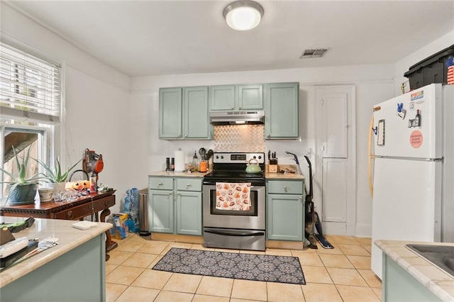 kitchen featuring stainless steel electric range, white refrigerator, light tile patterned floors, and tasteful backsplash