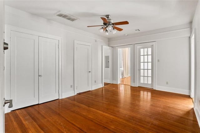 unfurnished bedroom with hardwood / wood-style floors, ceiling fan, and multiple closets