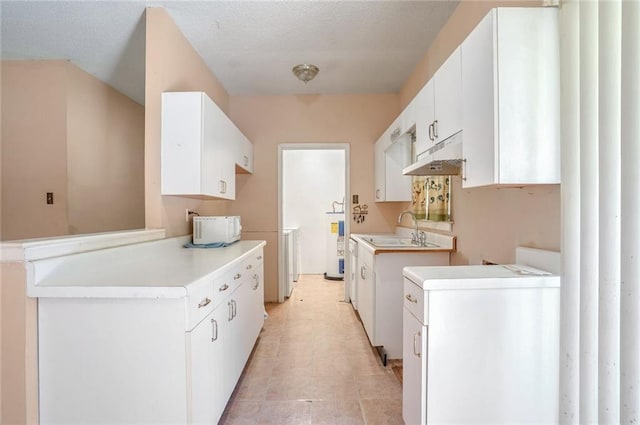 kitchen featuring a textured ceiling, washer / dryer, white cabinetry, and sink