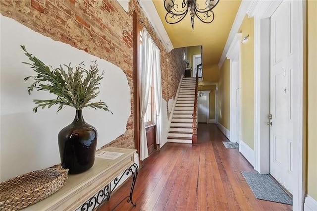 hall with a chandelier, hardwood / wood-style flooring, and brick wall