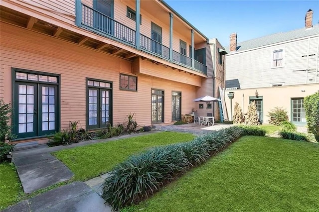 rear view of house featuring a patio area, a balcony, a yard, and french doors