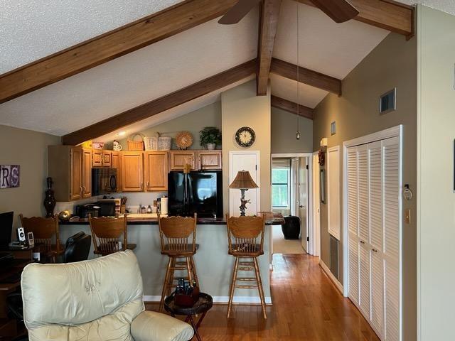 kitchen featuring a breakfast bar, hardwood / wood-style floors, vaulted ceiling with beams, black appliances, and kitchen peninsula