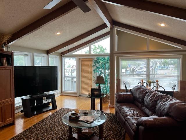 living room with lofted ceiling with beams, ceiling fan, a textured ceiling, and light hardwood / wood-style floors