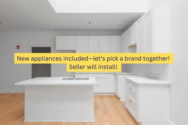 kitchen featuring light wood finished floors, a kitchen island with sink, a sink, light countertops, and white cabinetry