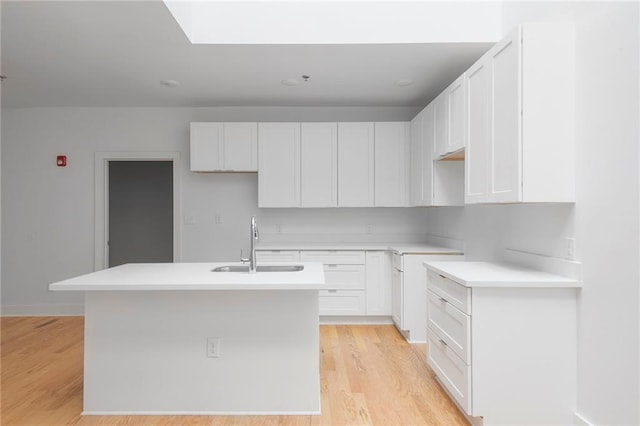 kitchen featuring a sink, light wood-type flooring, a center island with sink, and white cabinets