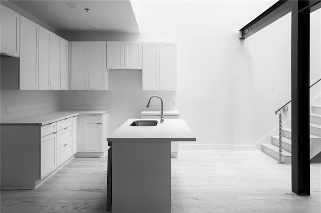 kitchen featuring an island with sink, baseboards, light wood-type flooring, and a sink