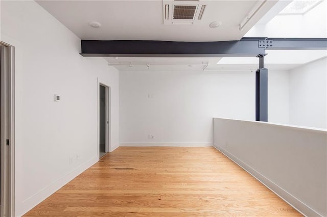 empty room with visible vents, track lighting, baseboards, beam ceiling, and light wood-style floors