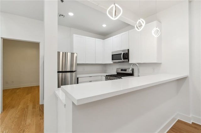 kitchen featuring white cabinetry, hanging light fixtures, stainless steel appliances, kitchen peninsula, and light wood-type flooring