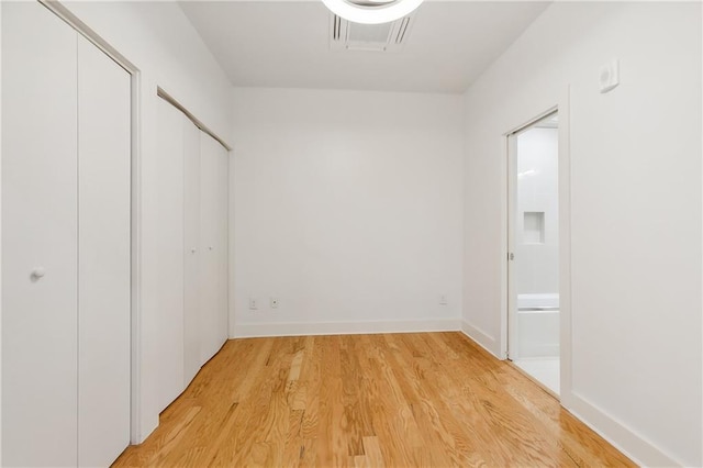 unfurnished bedroom featuring two closets, ensuite bathroom, and light wood-type flooring