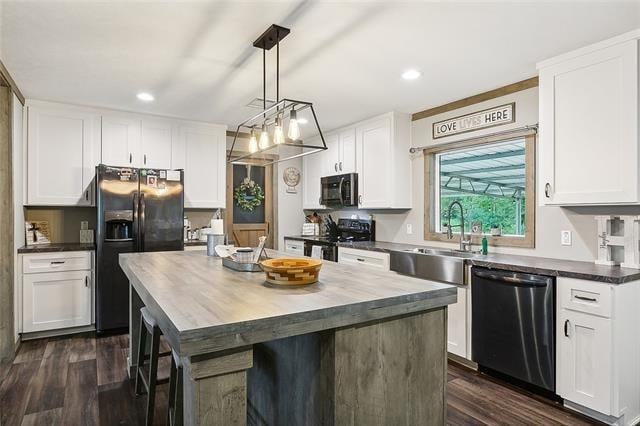 kitchen with dark hardwood / wood-style flooring, black appliances, decorative light fixtures, white cabinets, and a kitchen island